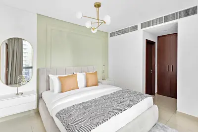 a white bedroom with a large bed with orange pillows at Silkhaus with Burj Khalifa view1BDR with modern amenities in Dubai