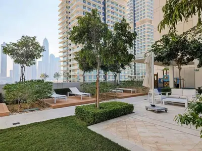 a park with white furniture and trees and buildings at Vogue Emaar Beachfront Beach Vista near JBR and Palm Jumeirah, One Bedroom Apartment with Balcony and Private Beach, Access to all Amenities in Dubai