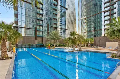 a large swimming pool with palm trees and tall buildings at Vogue Marina Gate near JBR Beach and Marina Mall, One Bedroom Apartment with Balcony and city skyline view, Access to all Amenities in Dubai