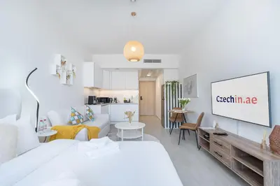 a white living room with a couch and a tv at Brand New & Modern Studio in JVC in Dubai