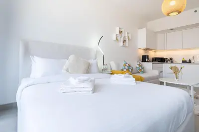 a white bedroom with a white bed with towels on it at Brand New & Modern Studio in JVC in Dubai