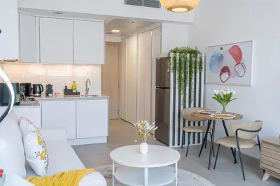 a kitchen and living room with white cabinets and a table at Brand New Vibrant Studio in JVC in Dubai
