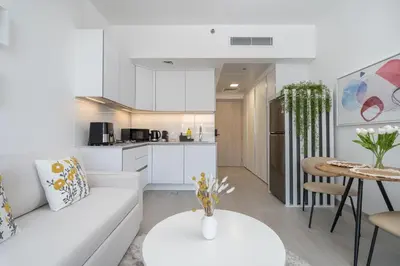 a white living room with a white couch and a table at Brand New Vibrant Studio in JVC in Dubai