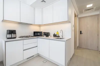 a white kitchen with white cabinets and a door at Brand New Vibrant Studio in JVC in Dubai