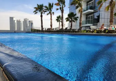 a large swimming pool with palm trees and a building at Full Golf View Studio in Damac Hills - Host & Stay in Dubai