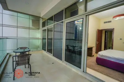 a room with a balcony with a bed and a table at Alashrafia Saray - Adorable 1BR in Sports City in Dubai