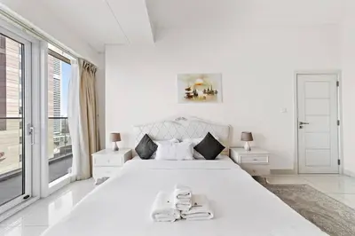 a white bedroom with a large white bed and a window at StoneTree - DAMAC Heights 1 BR - Amazing Facilities in Dubai
